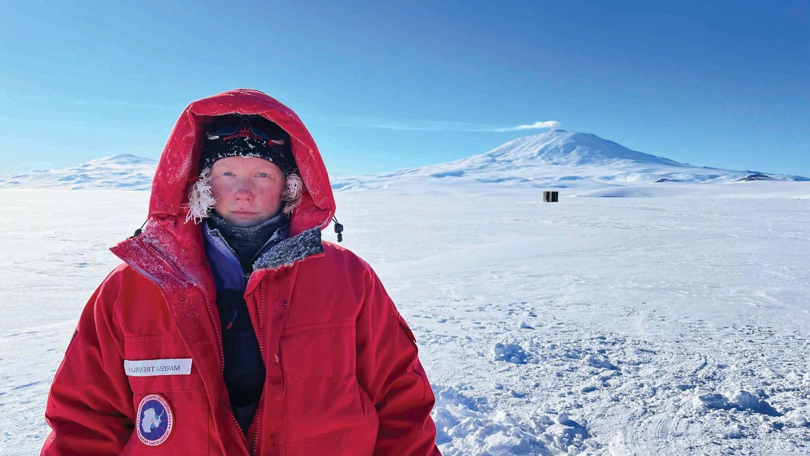 玛丽莎Tremblay在南极洲报道. 她穿着一件大红色大衣，戴着兜帽.